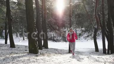 在寒冷的冬季森林里慢跑的女跑步者穿着温暖的运动服装和手套。